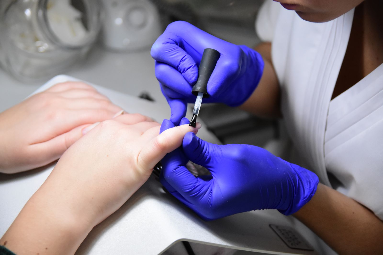 Classic manicure: Close-up of a manicurist applying nail polish wearing purple gloves in a salon.