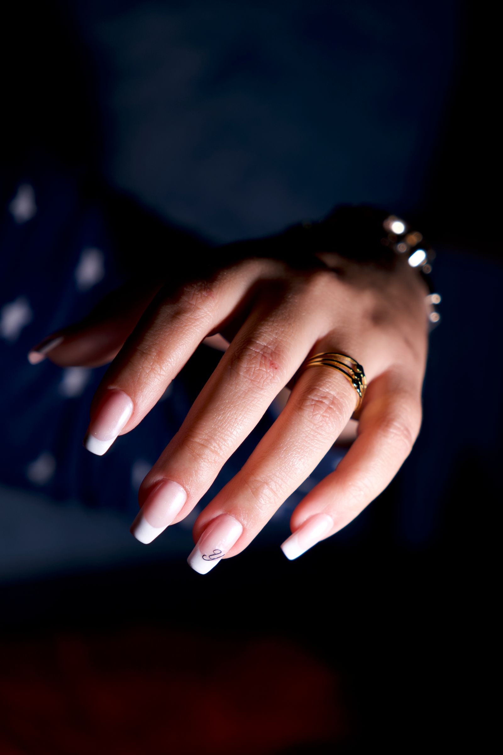 Bridal nude: A close-up of a woman's hand showcasing elegant rings and a delicate manicure in soft lighting.