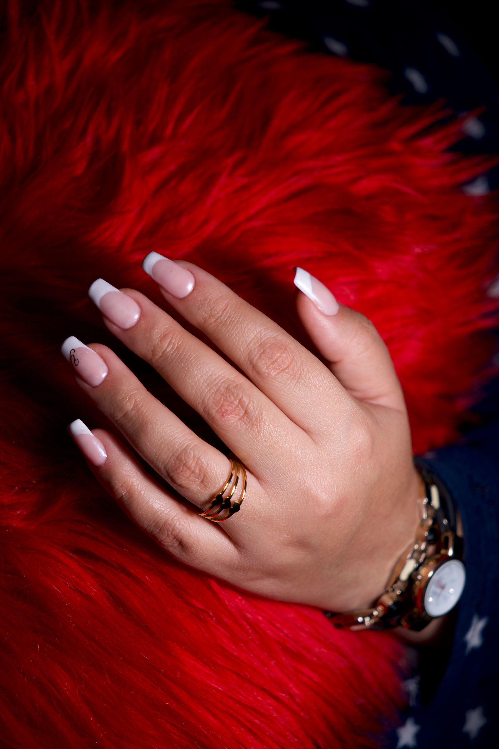 Glossy almond set: Close-up of a hand with French manicure adorned with rings and a gold watch.